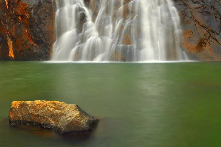 Base of a waterfall meeting a green pool with a rock